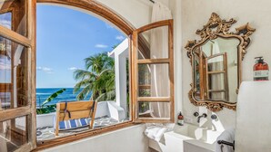 A bathroom with a view of the ocean, a wooden bench, a large ornate mirror, and a white sink. - Nosara Beach Hotel (Nosara)