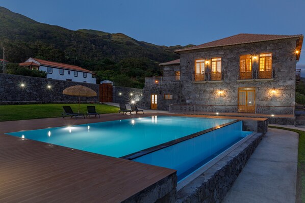 A stone building with a swimming pool, outdoor seating, and a mountain backdrop.