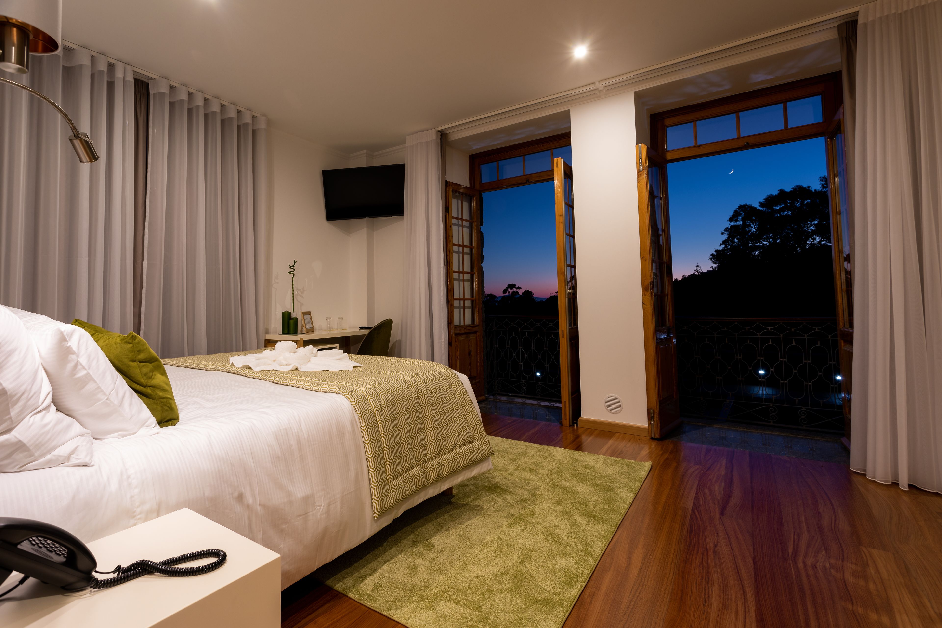 Ein Schlafzimmer mit Bett, Nachttischtelefon und Blick ins Freie durch eine Glastür.
