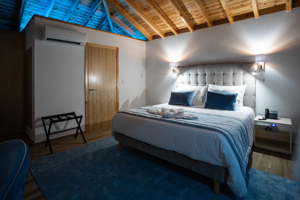 Ein Schlafzimmer mit Bett, Nachttischen, einer Bank und einer Decke mit Holzbalken.