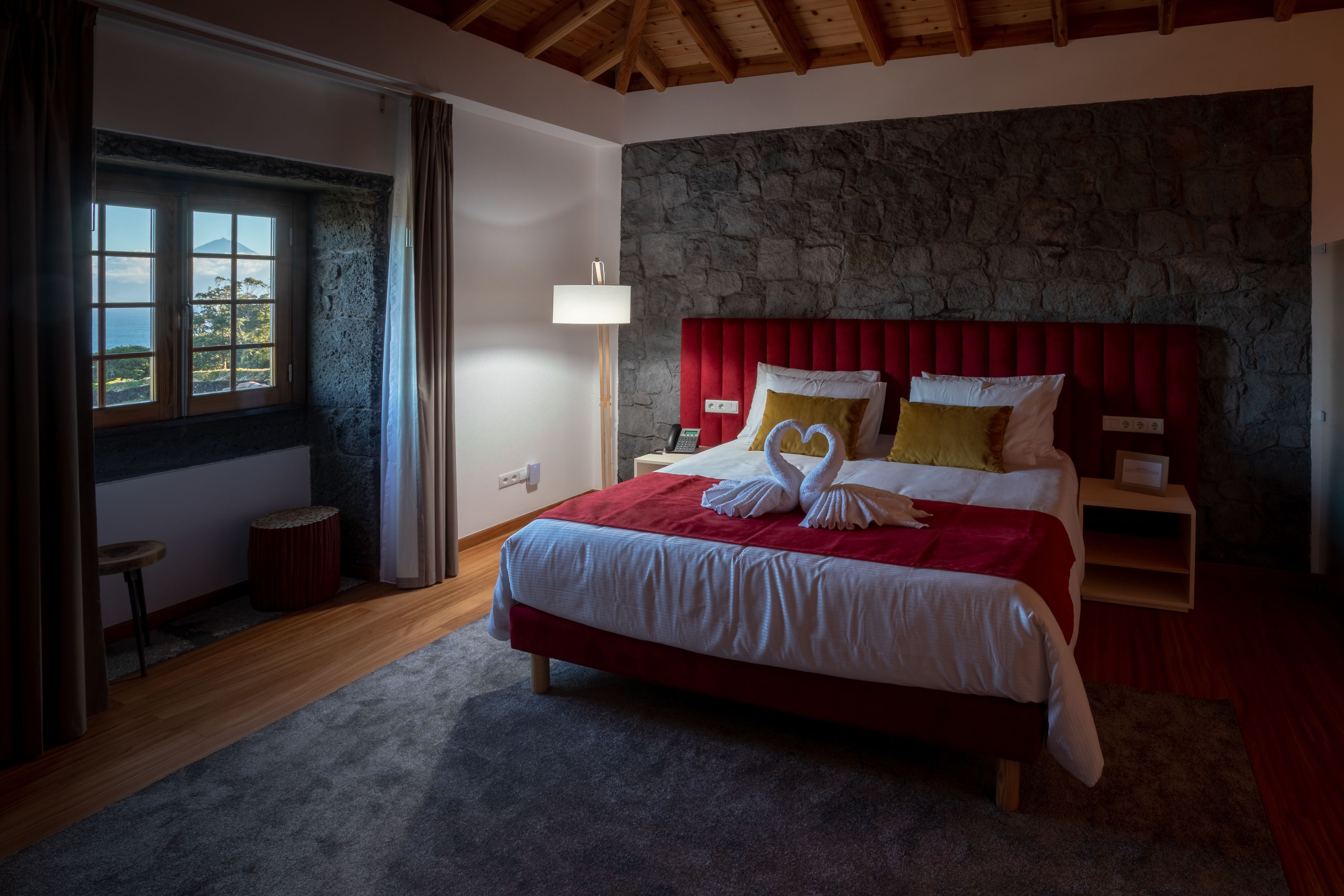 Ein Schlafzimmer mit Stehwand, einem roten Kopfteil, einem Bett mit weißen Leinen und einem Fenster mit Vorhängen.