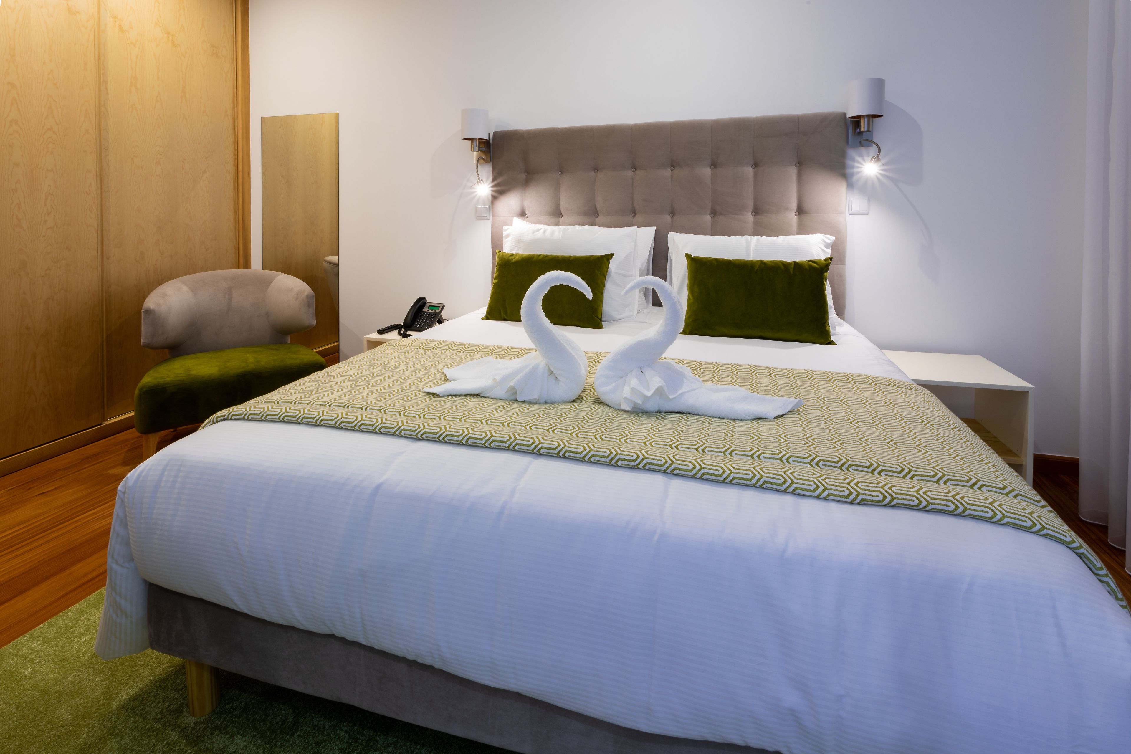 A neatly made bed with a patterned bedspread, two green pillows, and two swan-shaped towels.