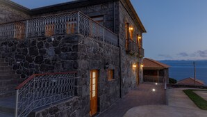 A stone building with a balcony, a wooden door, and a view of the sea. - Quinta da Magnólia (Velas)