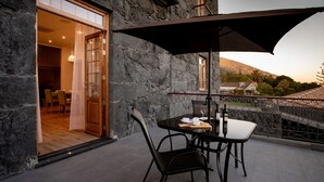 A balcony with a table and chairs, a large umbrella, and a view of a town and hills in the background. - Quinta da Magnólia (Velas)