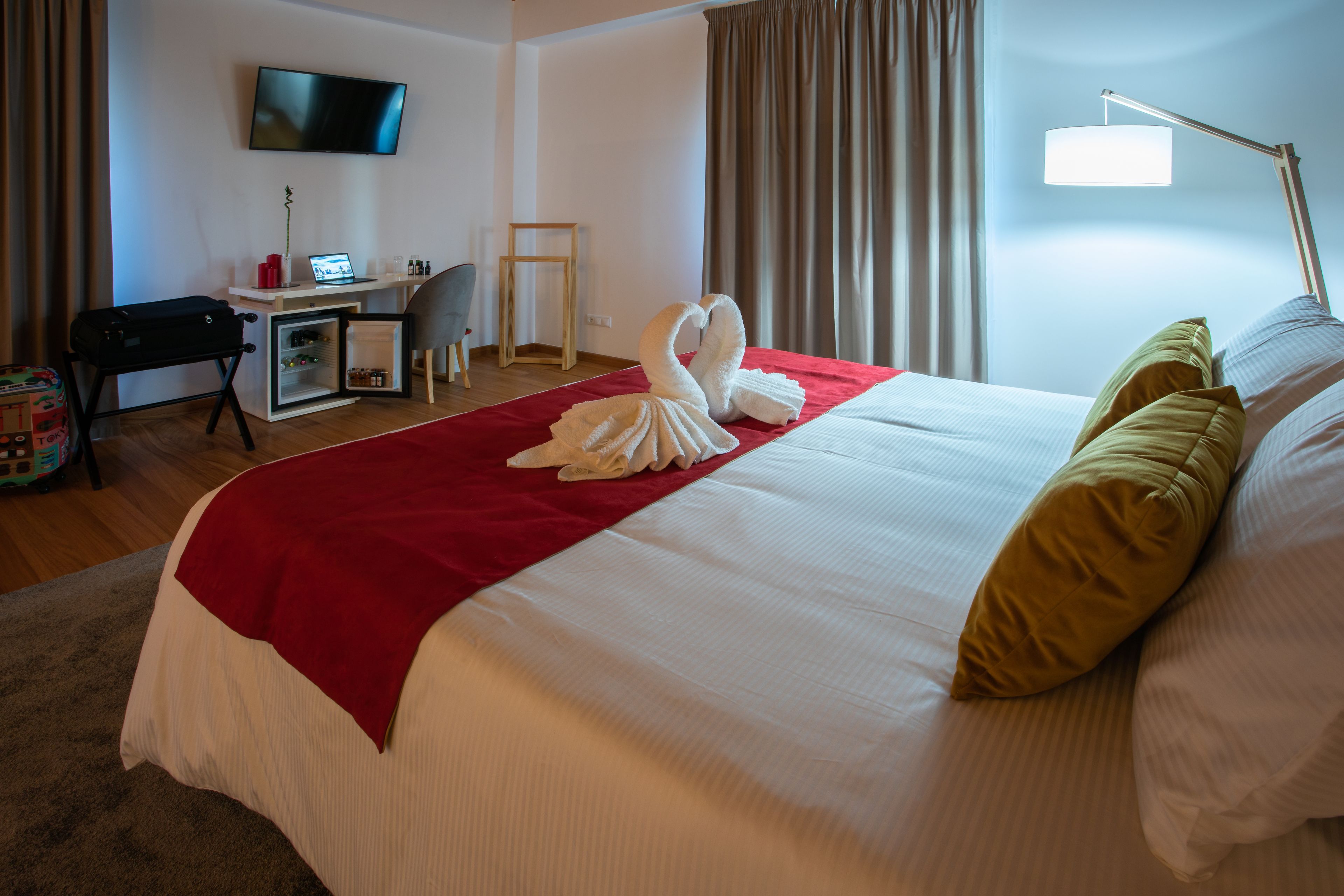 A hotel room with a bed, a desk, a chair, a TV, and a lamp.