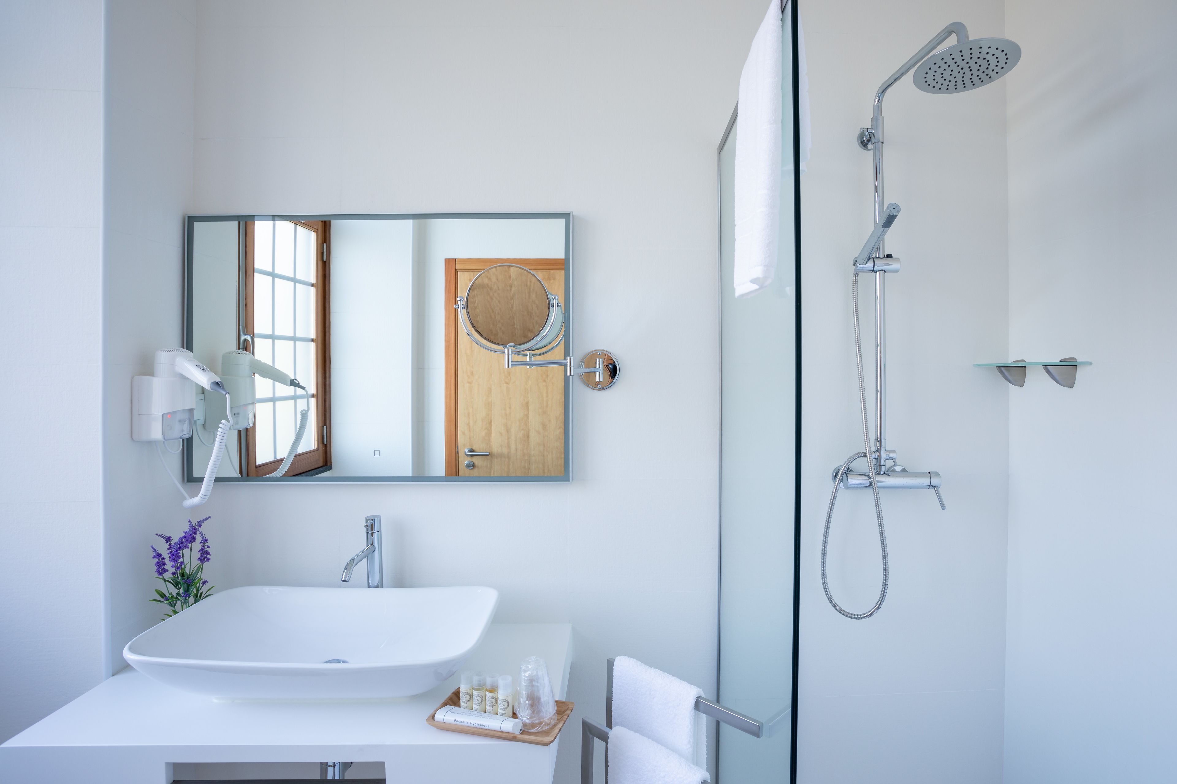 Een moderne badkamer met een wit wastafelmeubel, een spiegel, een douche en een handdoekrek.