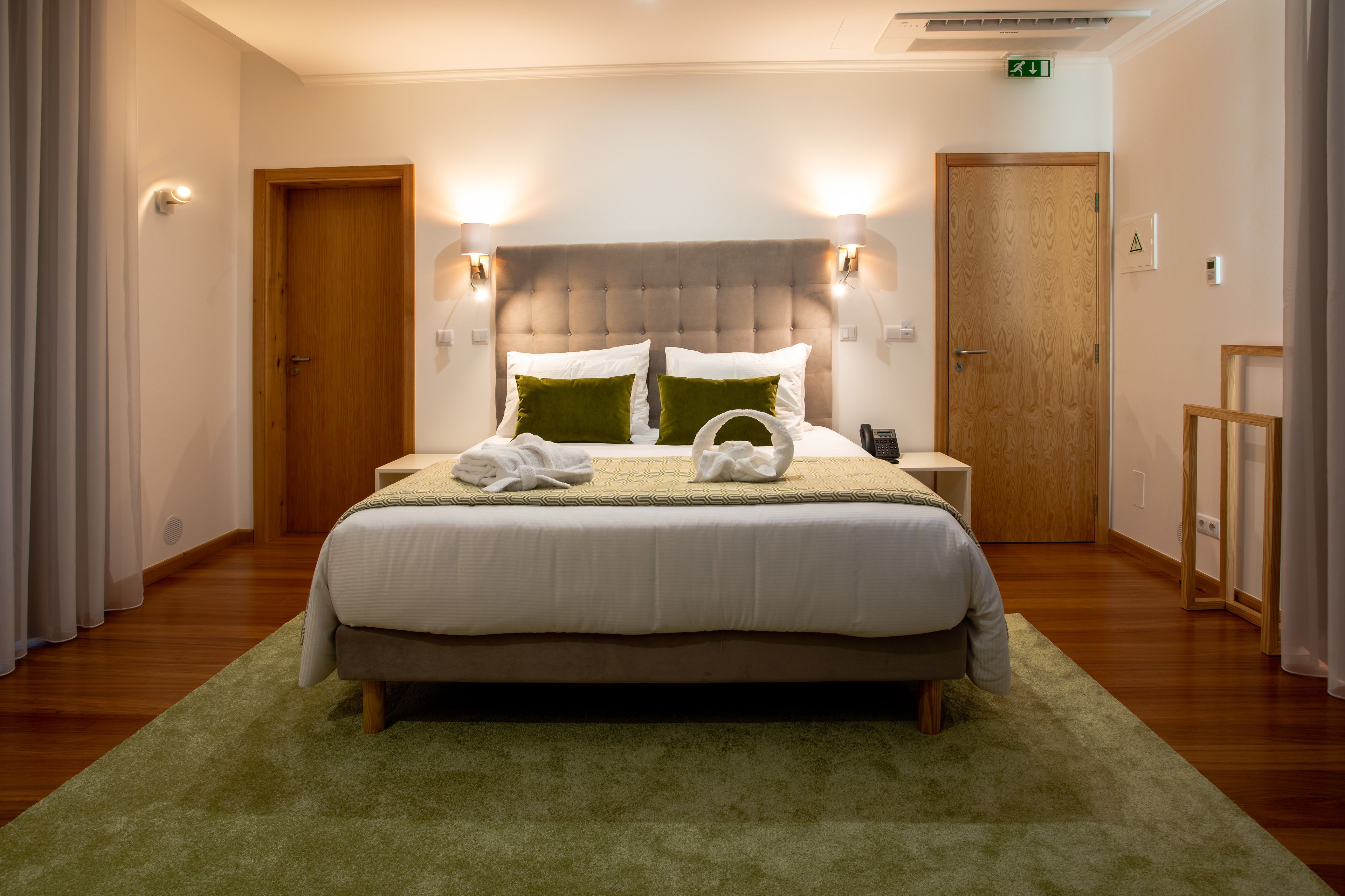 A neatly made bed with a green throw, a wooden headboard, and two bedside lamps.