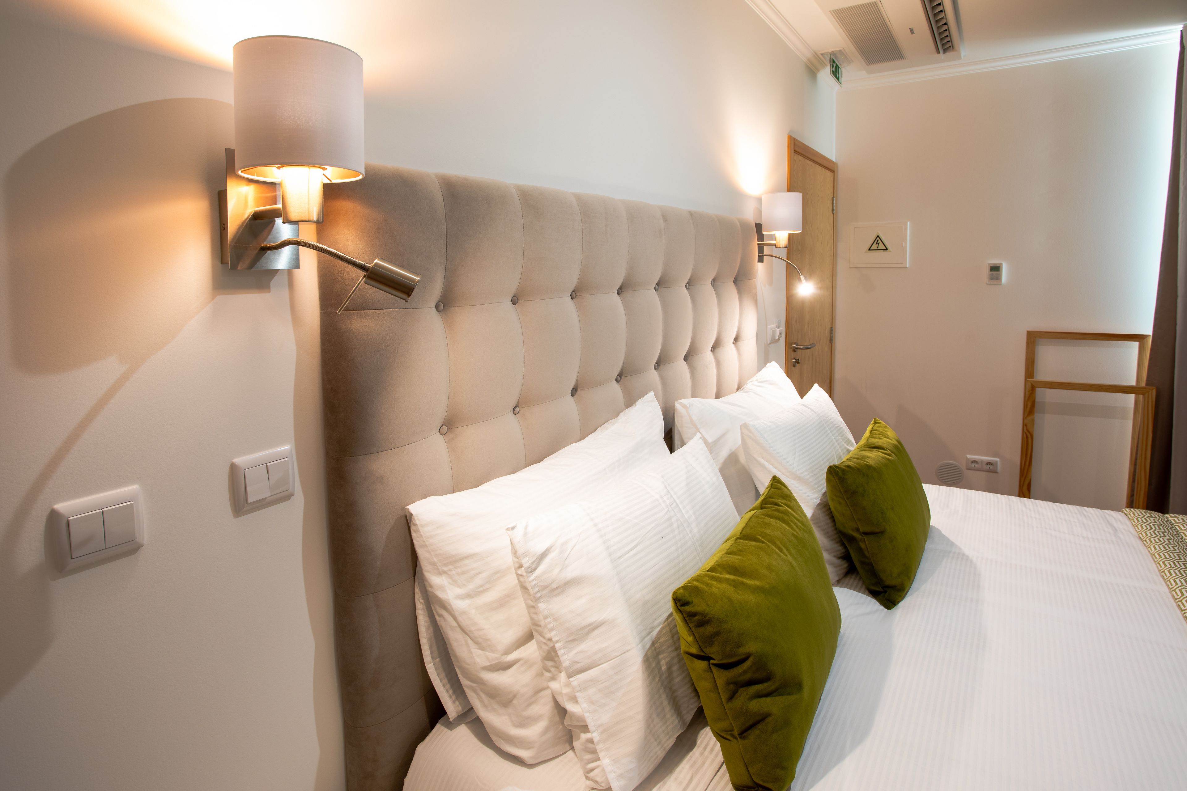 A hotel room with a tufted headboard, white bedding, and green pillows.