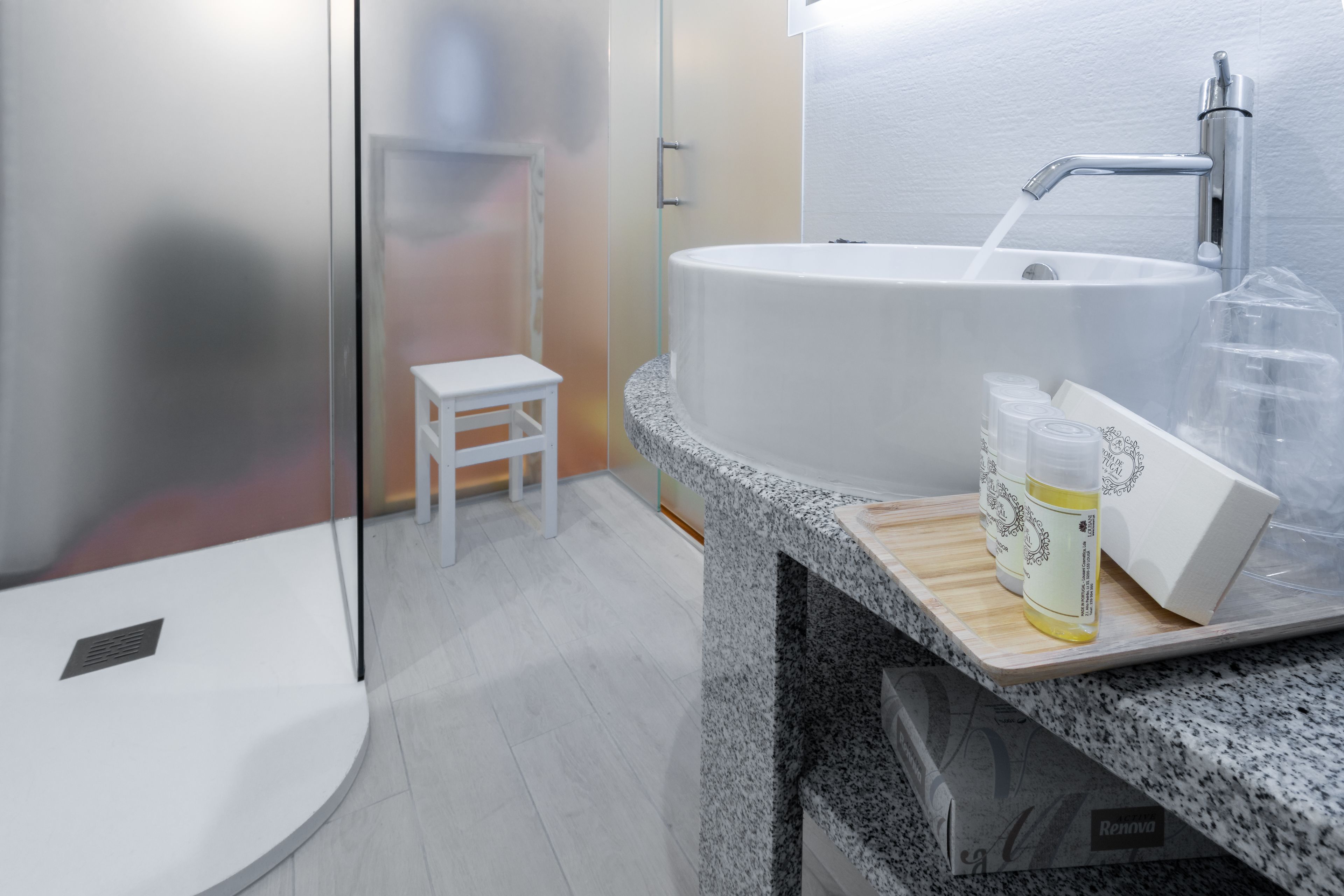 A modern bathroom with a large freestanding bathtub, a small white stool, and a wooden shelf with toiletries.