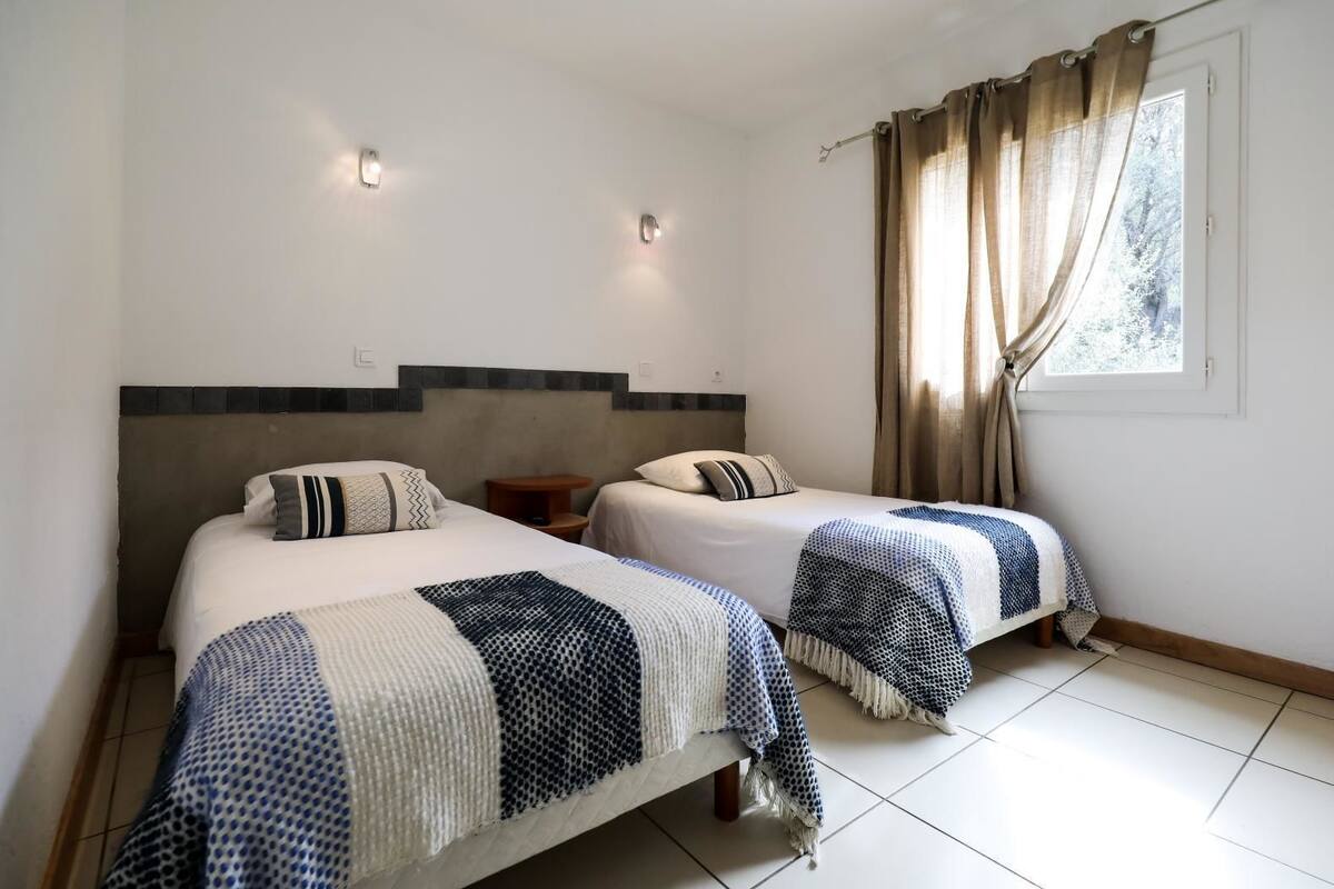 A hotel room with two beds, a small table, and a window with curtains.