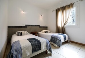 A hotel room with two beds, a small table, and a window with curtains. - Hotel Macchie E Fiori (Pianotolli-Caldarello)