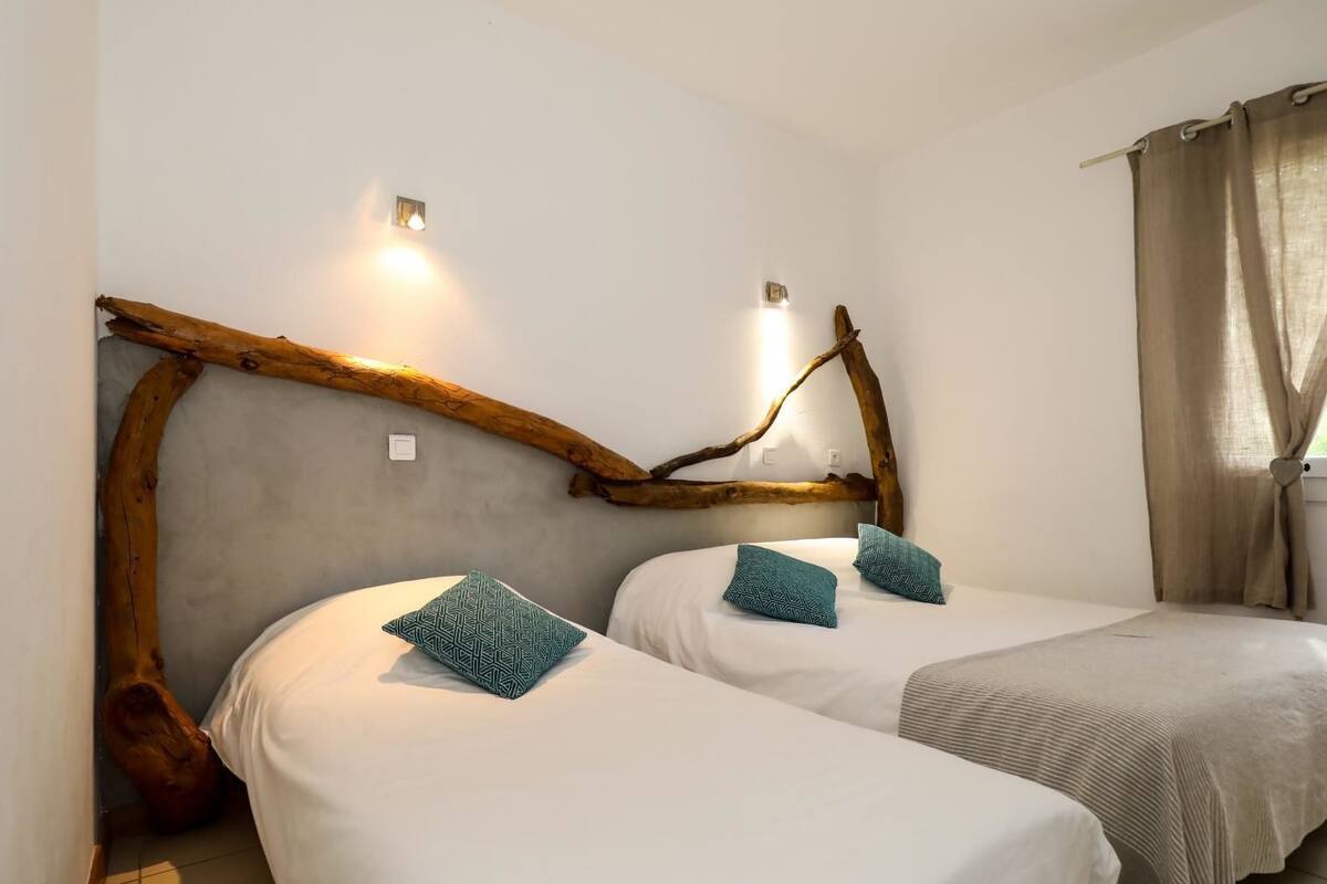 A room with two beds, each with a white mattress and teal pillows, and a wooden branch headboard.