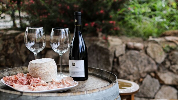 A rustic outdoor setting with a wooden barrel table, two wine glasses, a bottle of wine, and a plate of cured meats. - Hotel Macchie E Fiori (Pianotolli-Caldarello)