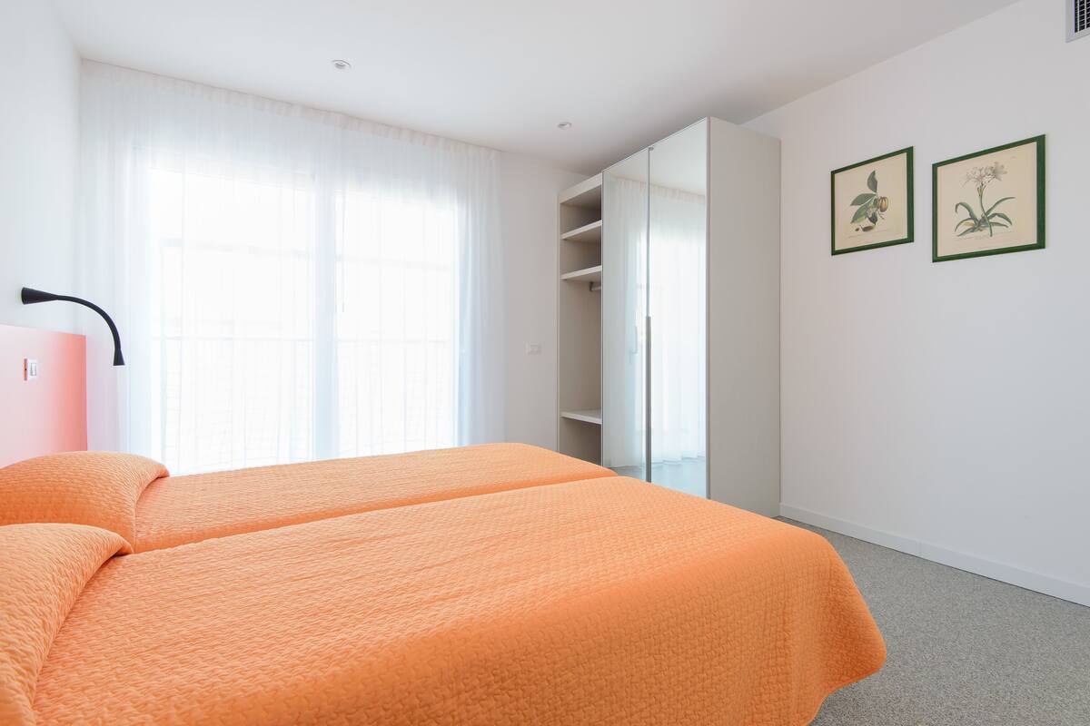 A bedroom with two beds, a wardrobe, and two framed botanical prints on the wall.