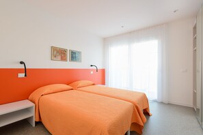 A hotel room with two beds, a bench, a painting, and a large window with curtains. - Residenza Edda (Lignano Sabbiadoro)