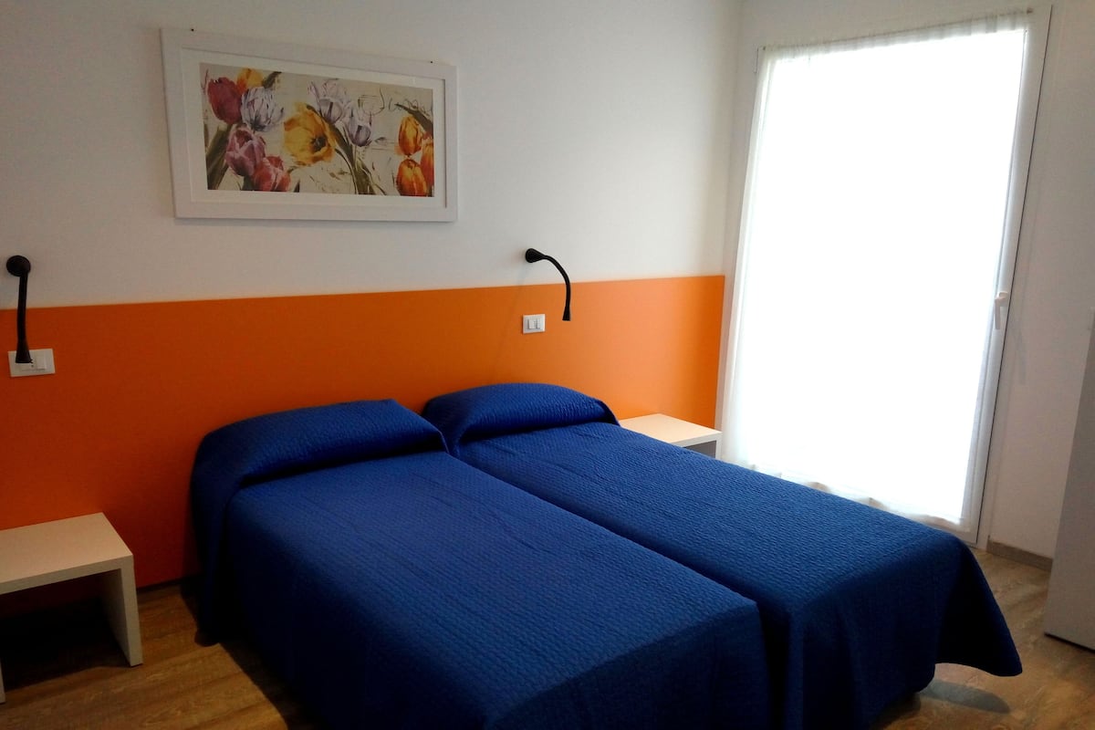 A room with two beds, a painting on the wall, a bedside table, and a window.