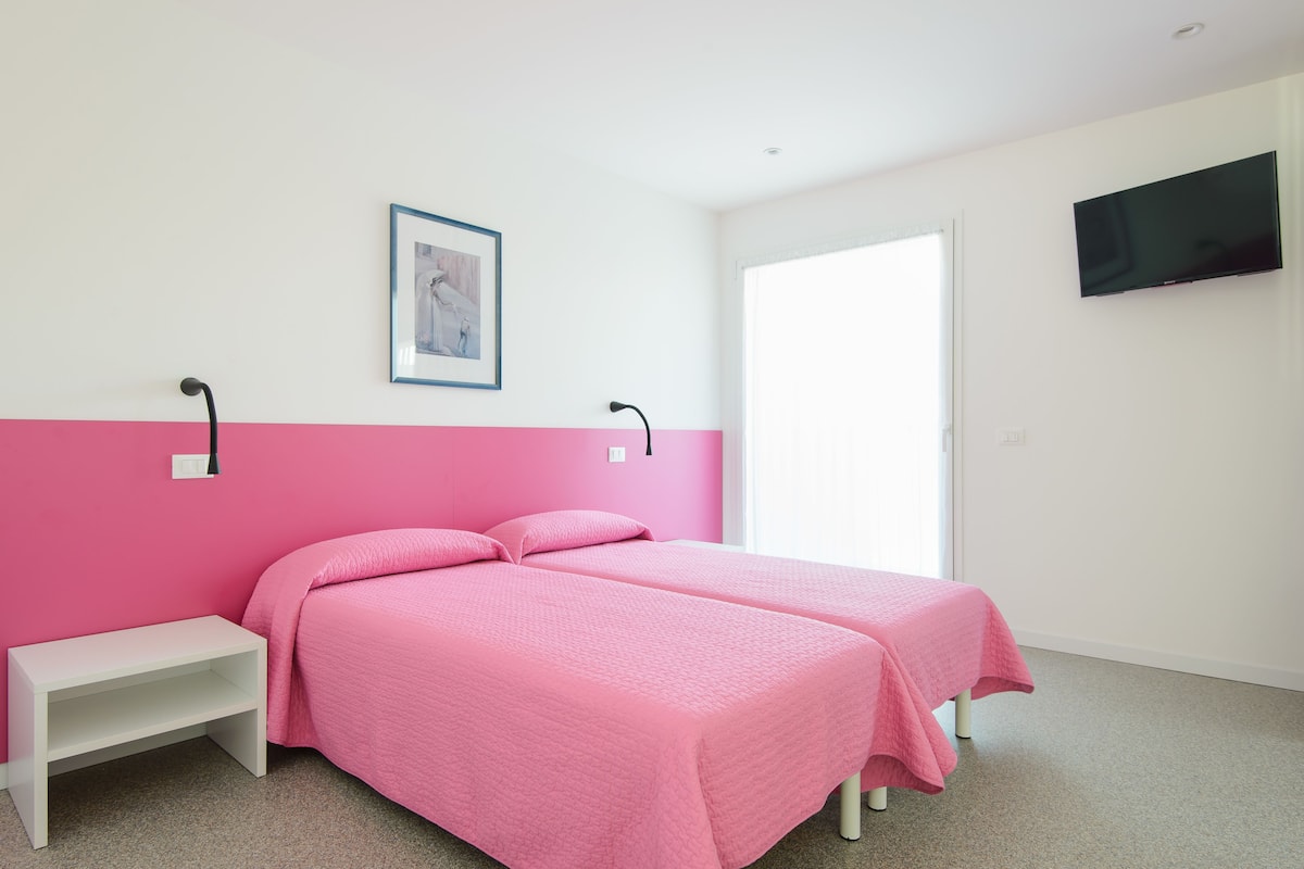 A room with two beds, a bench, a TV, and a framed picture on the wall.