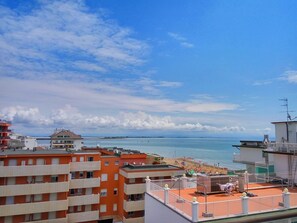 A coastal cityscape with a view of the sea, featuring multi-story buildings with balconies, a beach with umbrellas, and a clear sky. - Residenza Edda (Lignano Sabbiadoro)