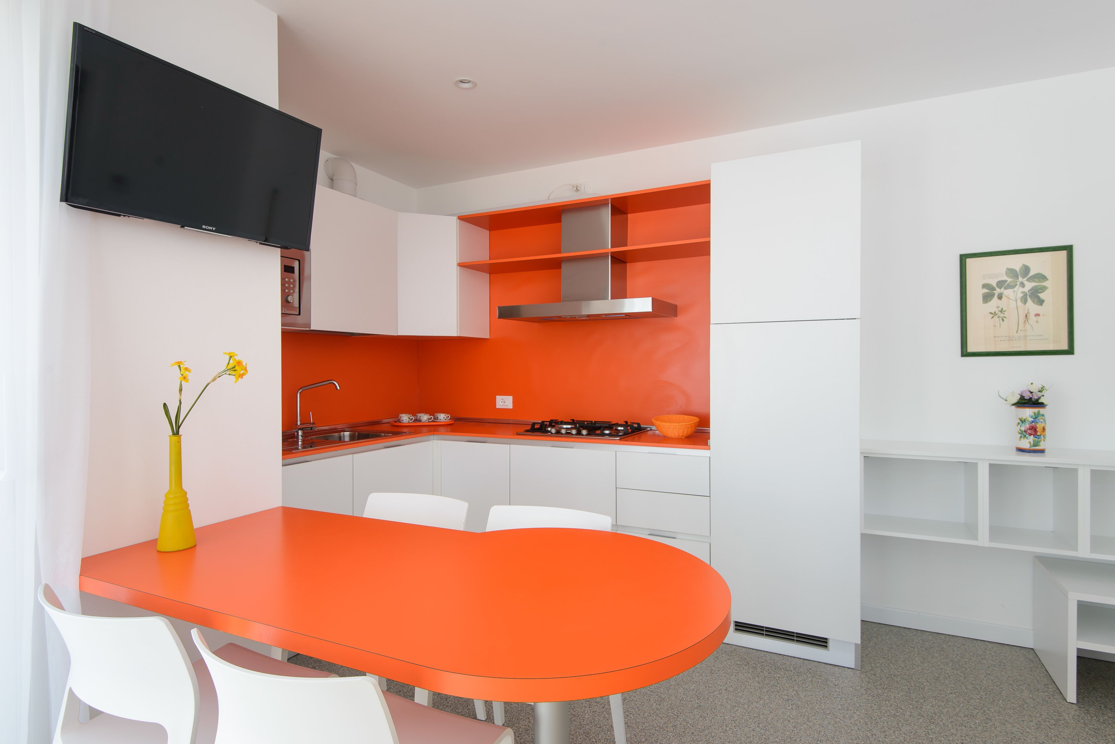 Een moderne keuken met witte kastjes, een oranje aanrechtblad en een ingebouwde kookplaat.