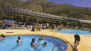A pool area with multiple swimming pools, a beach, and a mountainous backdrop. - Hostal El Bouquet (La Vall de Boi)