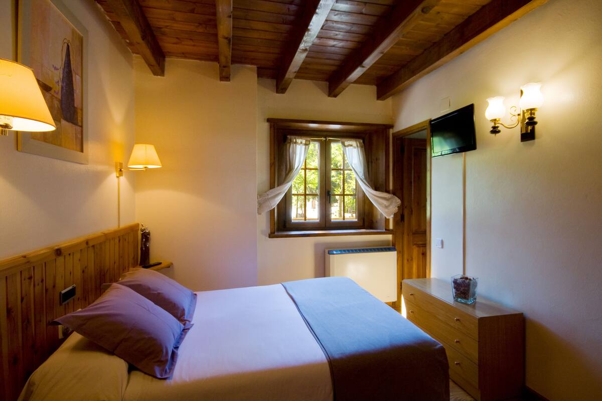 Un dormitorio con cabecera de madera, una cama con dos almohadas, un tocador, un espejo y una ventana con cortinas.