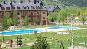 A hotel with a pool area, outdoor play equipment, and a mountainous backdrop. - Hostal El Bouquet (La Vall de Boi)