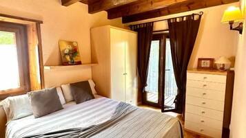 A bedroom with a wooden ceiling, a bed with a striped bedspread, a dresser, and a window with curtains.