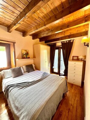 A bedroom with a wooden ceiling, a bed with a striped bedspread, a dresser, and a window with curtains. - Hostal El Bouquet (La Vall de Boi)