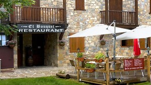 A stone building with a wooden balcony and outdoor seating area with umbrellas. - Hostal El Bouquet (La Vall de Boi)