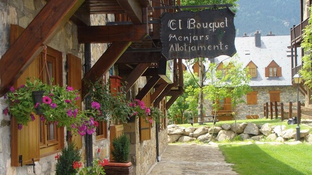 A stone building with wooden beams and a sign reading "El Bouquel Menjars Allotjaments". - Hostal El Bouquet (La Vall de Boi)