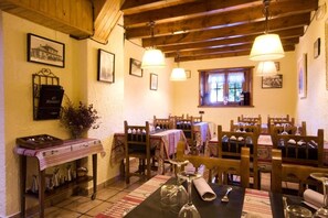 A dining area with wooden tables, chairs, and hanging lamps. - Hostal El Bouquet (La Vall de Boi)