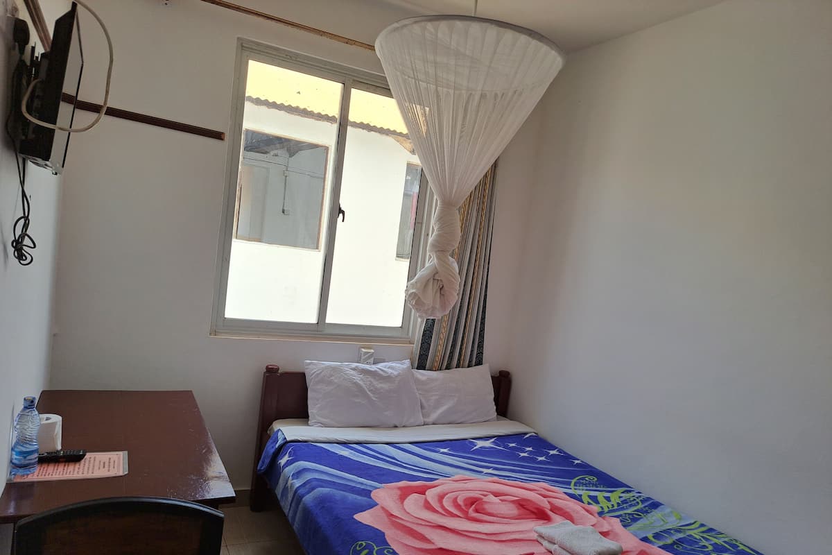 Un dormitori amb llit, escriptori, cadira, finestra amb cortines i mosquiter a penjar.