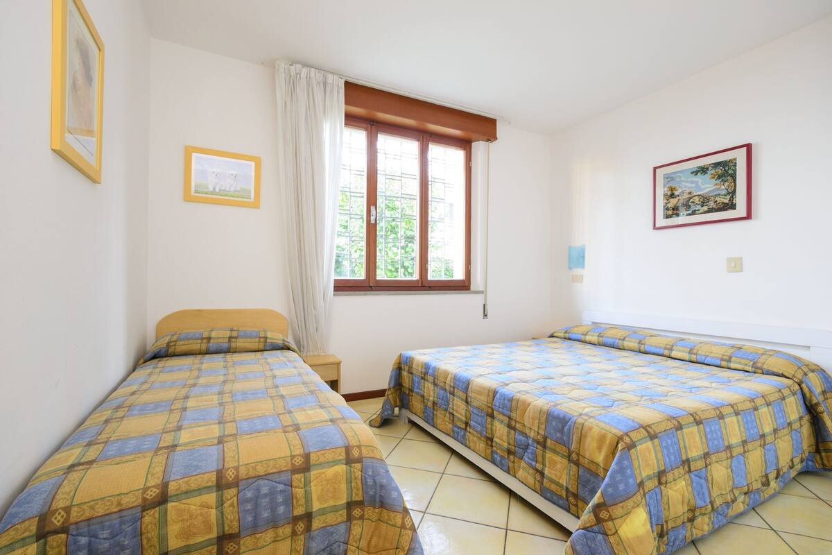 A room with two beds, a window with curtains, and framed pictures on the walls.