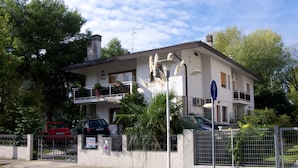A two-story building with a balcony, a car parked in front, and a no parking sign. - Villa Erica (Lignano Sabbiadoro)