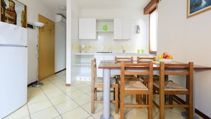 A compact kitchen with a dining table and chairs, a refrigerator, and a sink. - Villa Erica (Lignano Sabbiadoro)