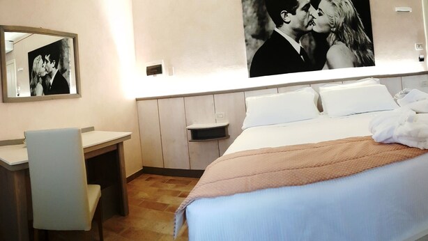 Une chambre d’hôtel comprenant un lit, un bureau, une chaise, un grand miroir et une armoire.