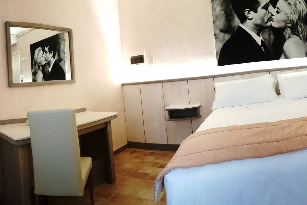 Une chambre d’hôtel comprenant un lit, un bureau, une chaise, un grand miroir et une armoire.