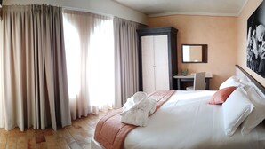 Une chambre d’hôtel avec un lit, un bureau, une chaise, un miroir et un tableau au mur.