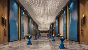 A hotel corridor with a marble floor, blue-tied tables with flowers, and a ceiling with hanging lights. - Radisson Ningbo Beilun (Ningbo)