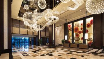 A spacious lobby with a checkered floor, large decorative chandeliers, and a reception area with a floral wall design.