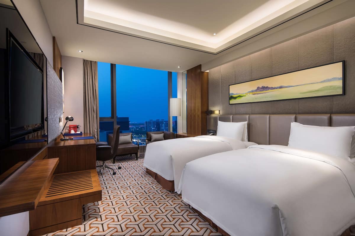 Een moderne hotelkamer met twee bedden, een bureau, een televisie en uitzicht op de stad.