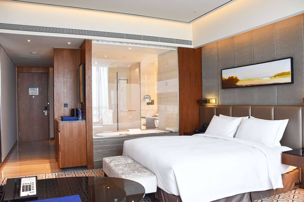 Een moderne hotelkamer met een groot bed, een bureau, een zithoek en een badkamer die zichtbaar is door een glazen deur.