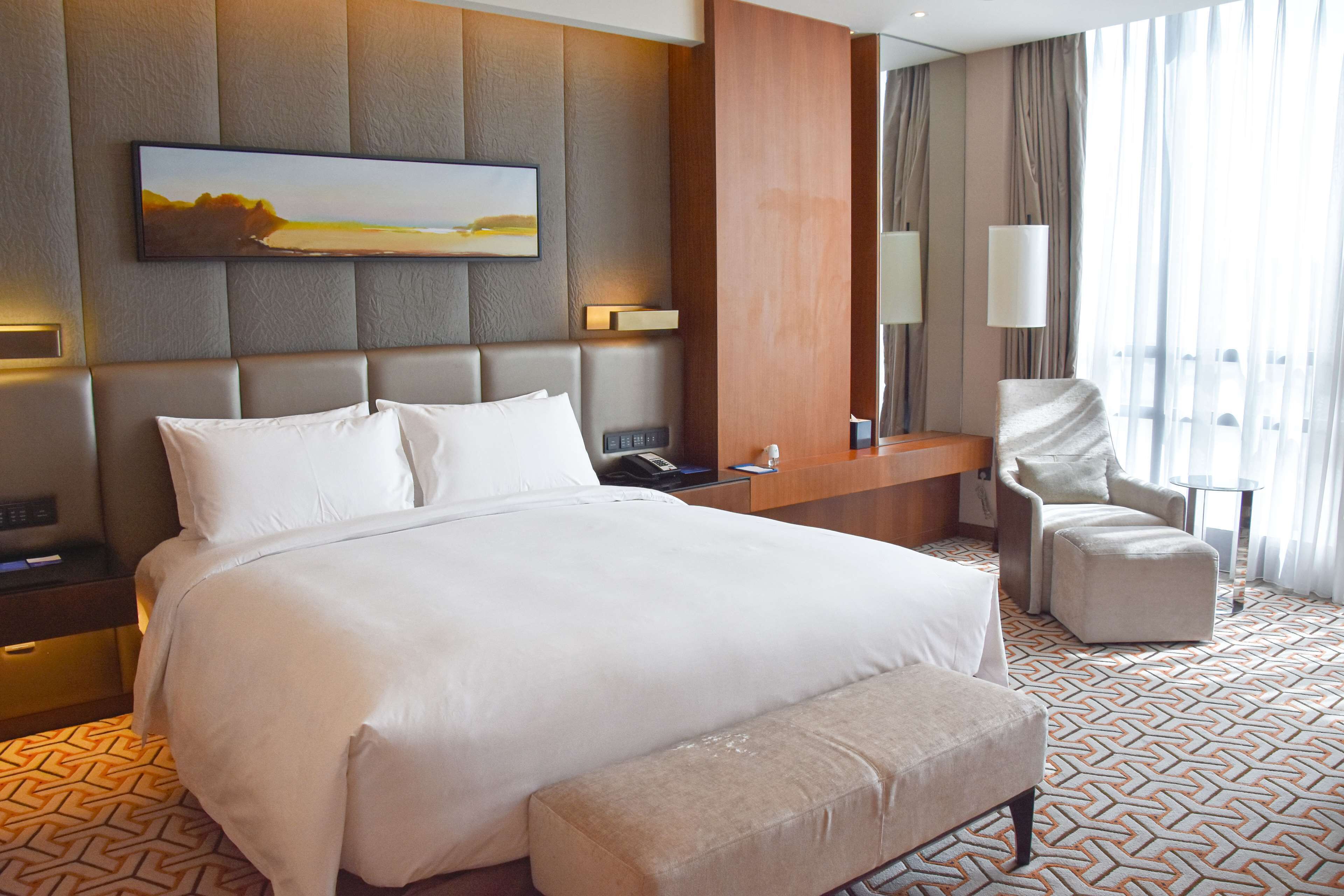 A hotel room with a large bed, a desk, a chair, and a painting on the wall.
