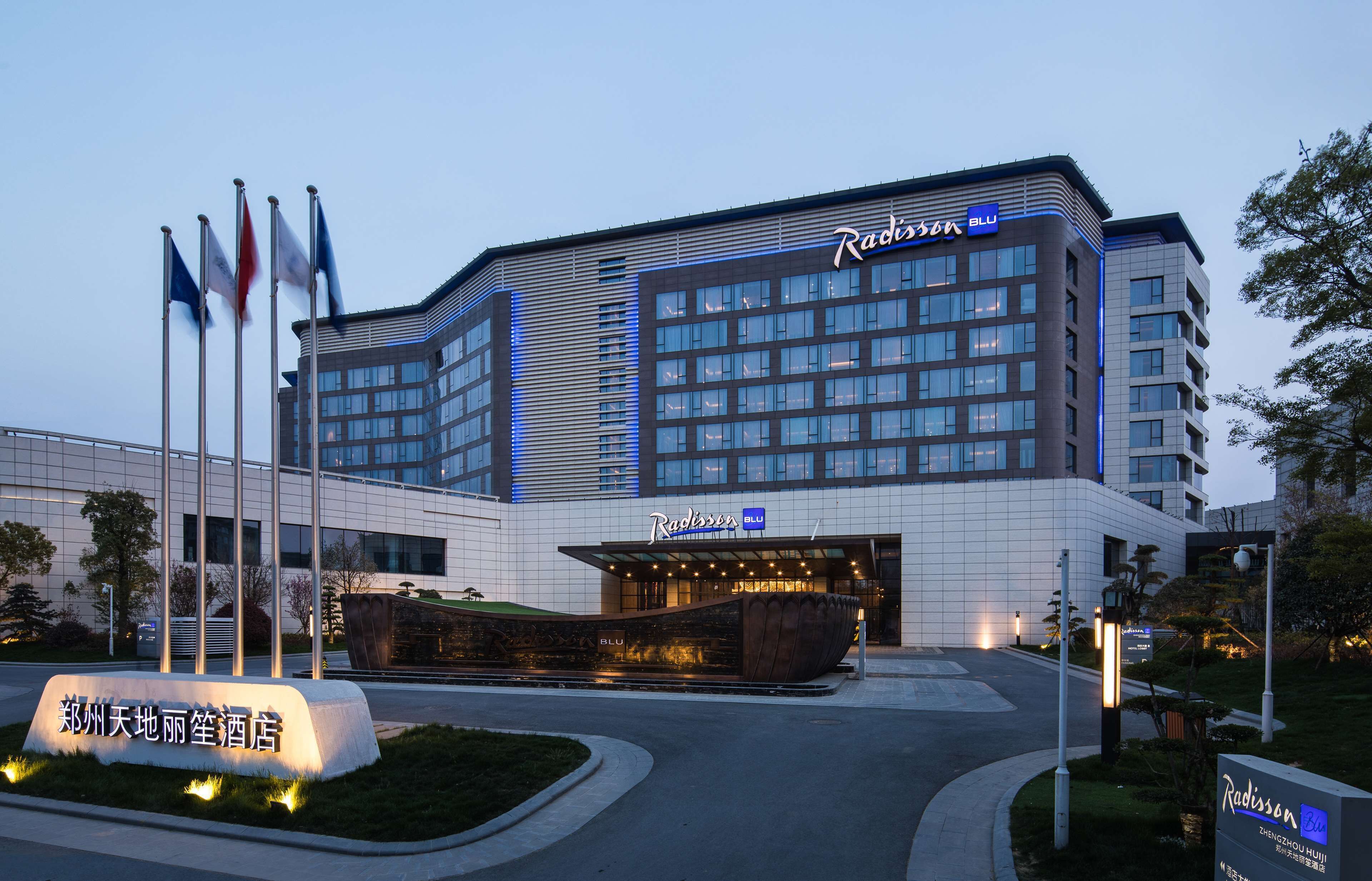 Un hotel Radisson Blu con fachada moderna, varias banderas y una entrada bien iluminada.