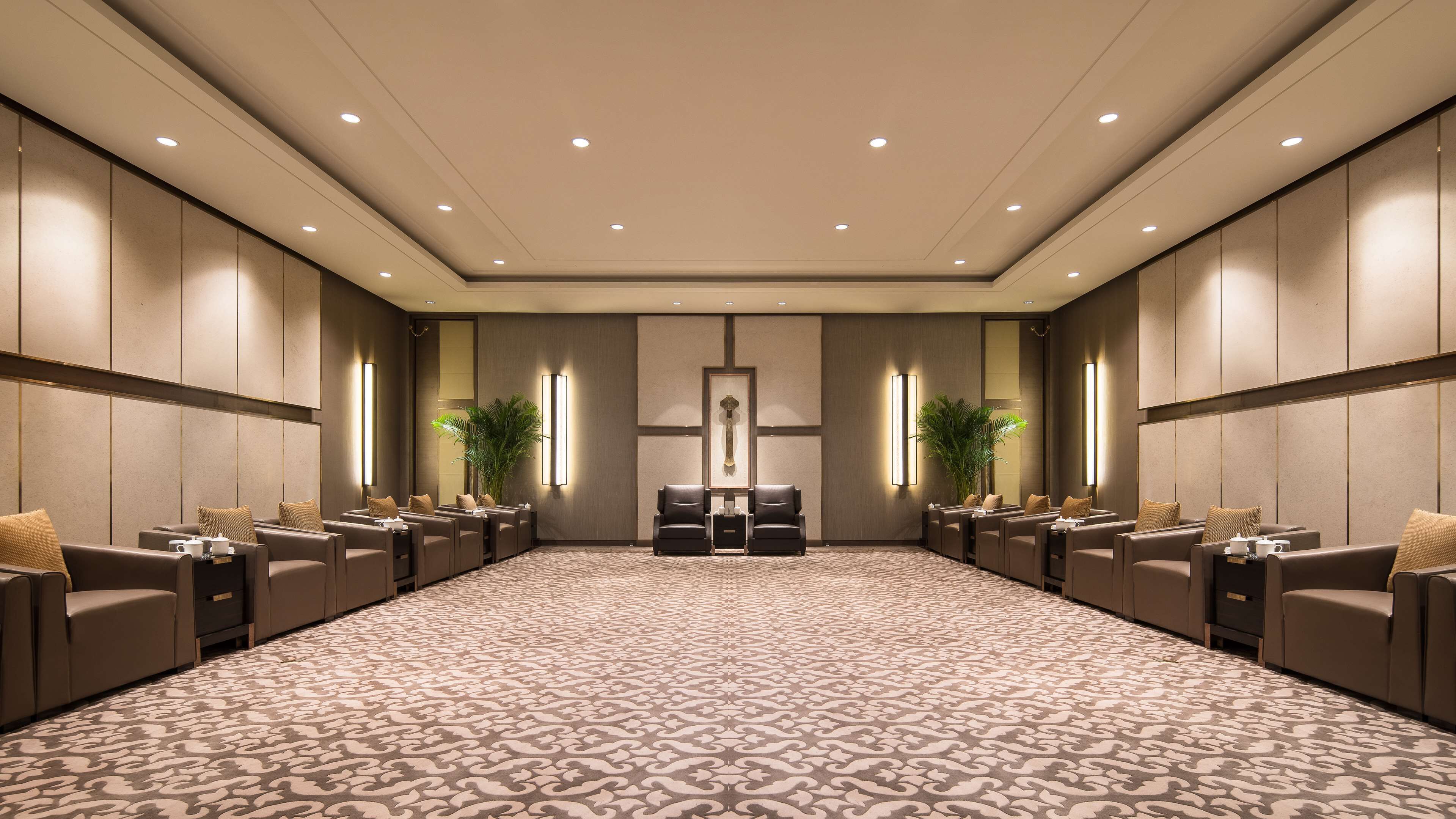 A spacious conference room with a patterned carpet, leather seating, and wall-mounted lighting.