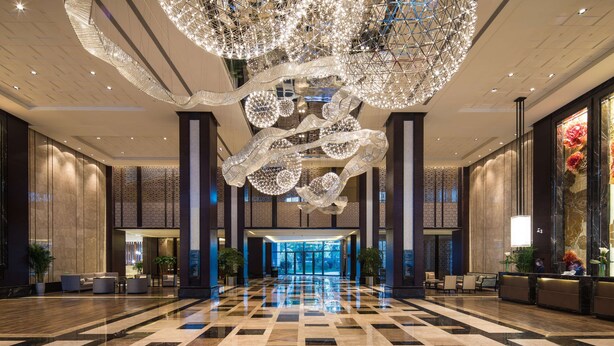 Eine geräumige Lobby mit Schachbrettmuster-Boden, einem großen Chandelier und einem Empfangstresen.