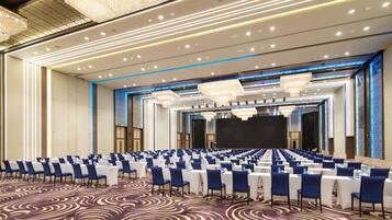 A large conference room with rows of tables and chairs, a stage, and a patterned carpet.