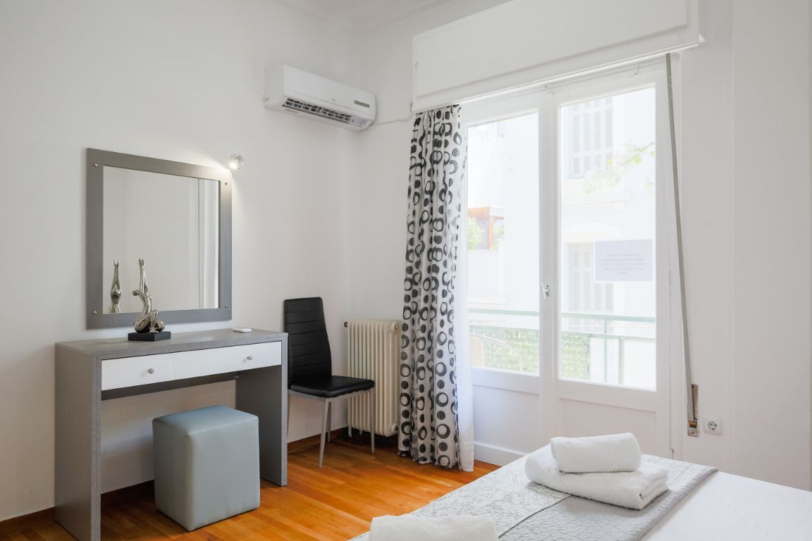 Un dormitorio con cama, escritorio con silla, radiador y ventana con cortinas.