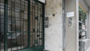Ein Gebäudeeingang mit einem grünen Metallgitter, einer Betonstütze und einem kleinen Schild.