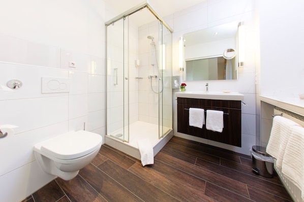 A modern bathroom with a glass-enclosed shower, a white toilet, and a dark wood vanity with a mirror. - Hotel Ochsen (Binzen)